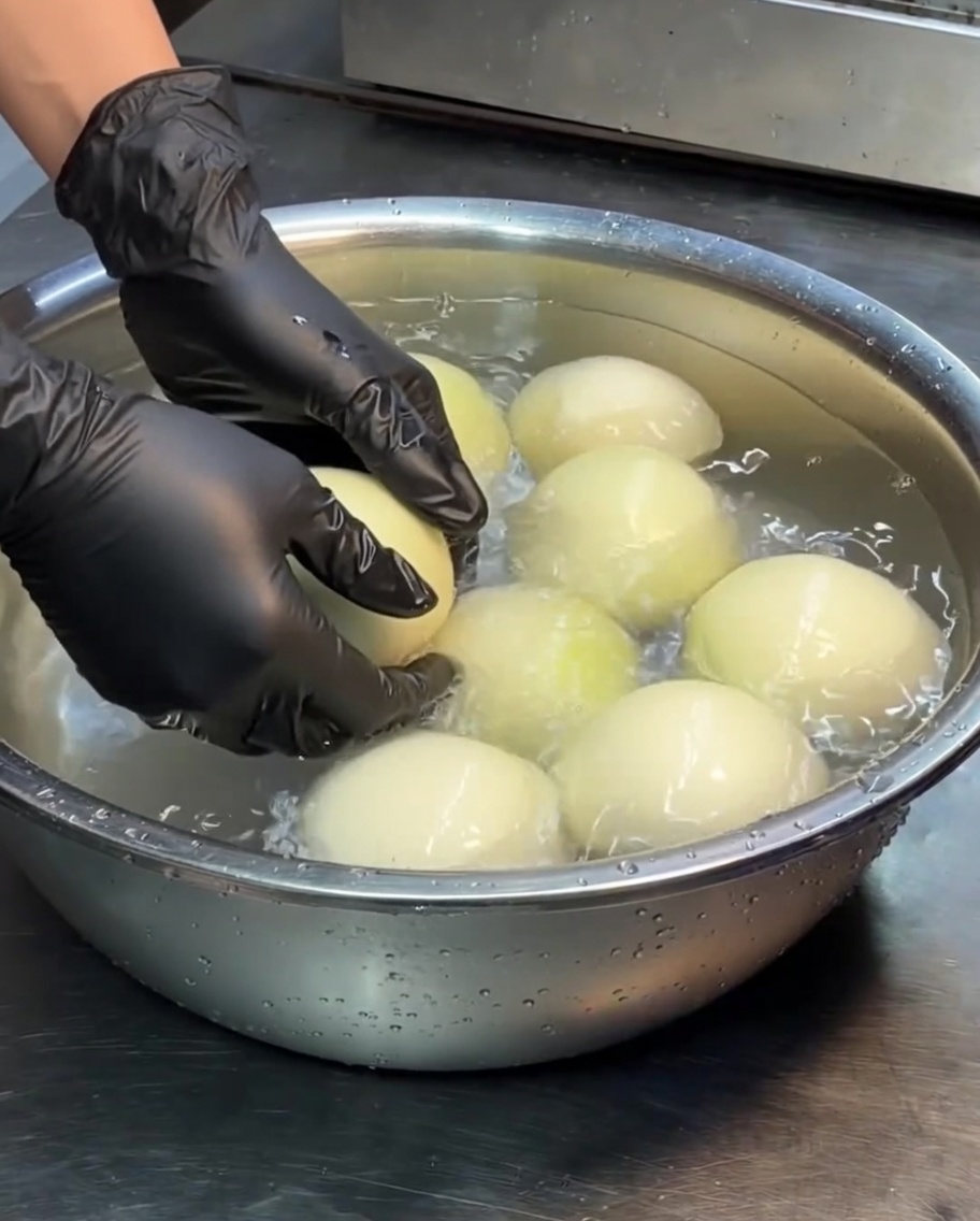 Ganze weiße Zwiebeln liegen in einem mit Wasser gefüllten Edelstahlbecken.