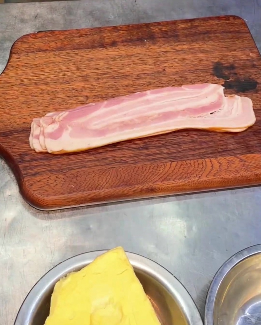 In Stücke geschnittener geräucherter Bacon liegt auf einem Holzschneidebrett.