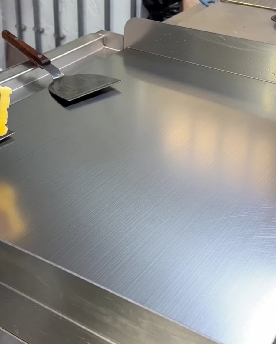 Gelbe Butter schmilzt und bedeckt die Oberfläche einer heißen Edelstahlgrillplatte.