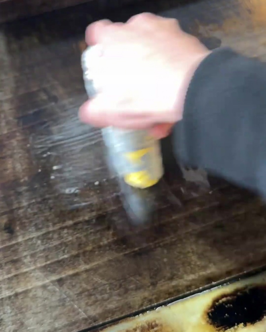 Eine Hand verteilt geschmolzene Butter auf der Oberfläche einer heißen Grillplatte.