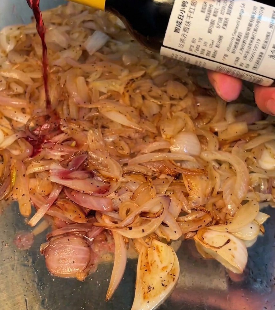 Ein Schuss Rotwein wird in die Pfanne zu den Zwiebeln gegossen.