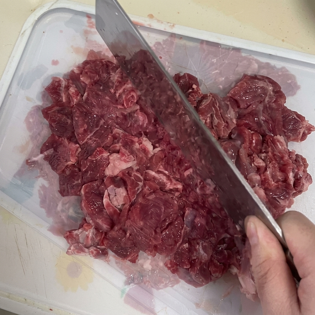 Rindfleisch wird mit einem Hackmesser auf einem Schneidebrett zerkleinert.
