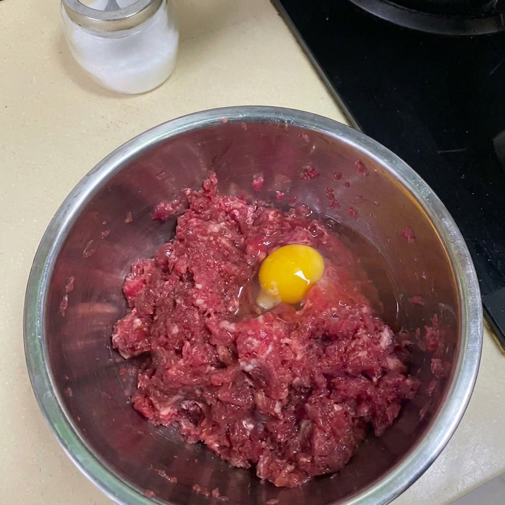 Hackfleisch wird in einer Metallschüssel mit Gewürzen und einem Ei vermengt.