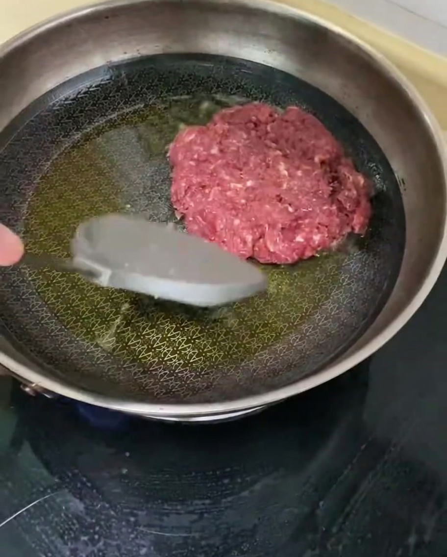 Ein gewürztes Rinderpatty brät in einer heißen Pfanne mit Öl.