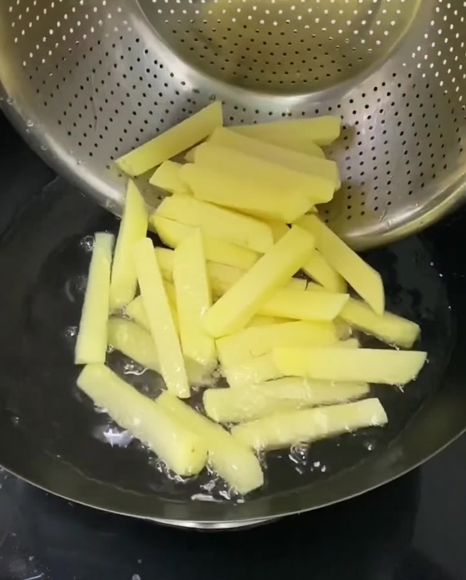 Kartoffelstifte in einem Nudelsieb, das in einem Topf mit heißem Wasser hängt.