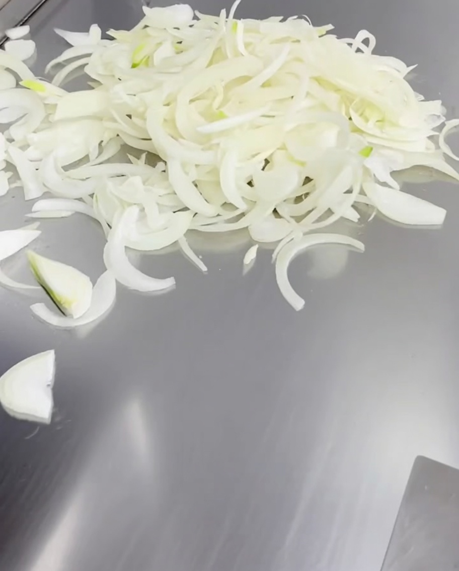 Dünn geschnittene weiße Zwiebelstreifen auf einer heißen Grillplatte.