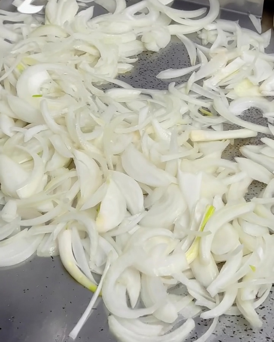 Geschmolzene Butter aus einem kleinen Topf über Zwiebeln auf einer heißen Grillplatte.