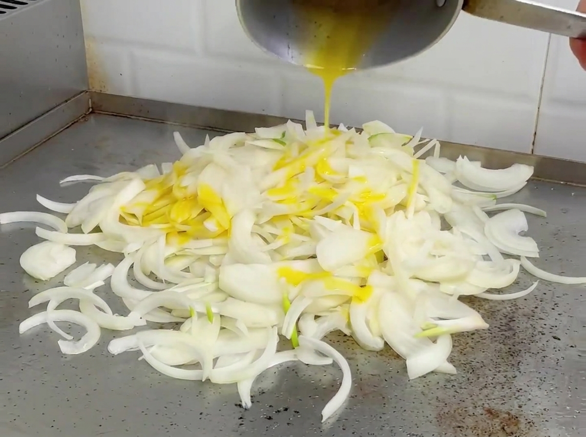 Zwiebeln werden auf einer heißen Platte angebraten, sie wirken weich und leicht gebräunt.
