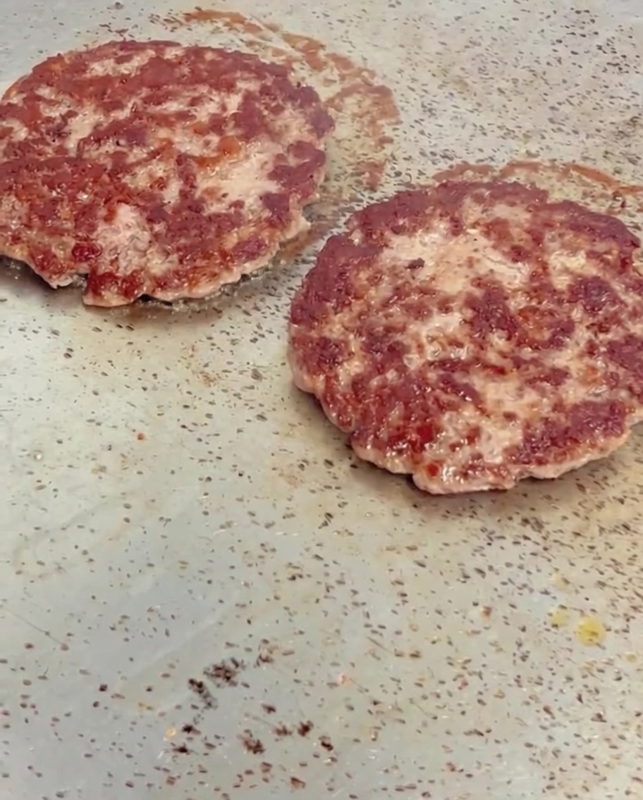 Käsescheiben schmelzen auf heißen, gebräunten Rindfleisch-Patties auf einer Grillplatte.