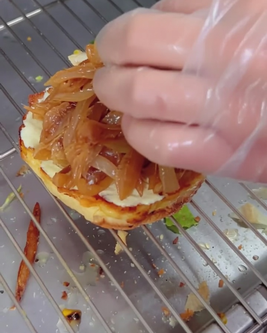 Karamellisierte Zwiebeln werden auf ein Brötchen geschichtet, darauf ein käsiges Patty.