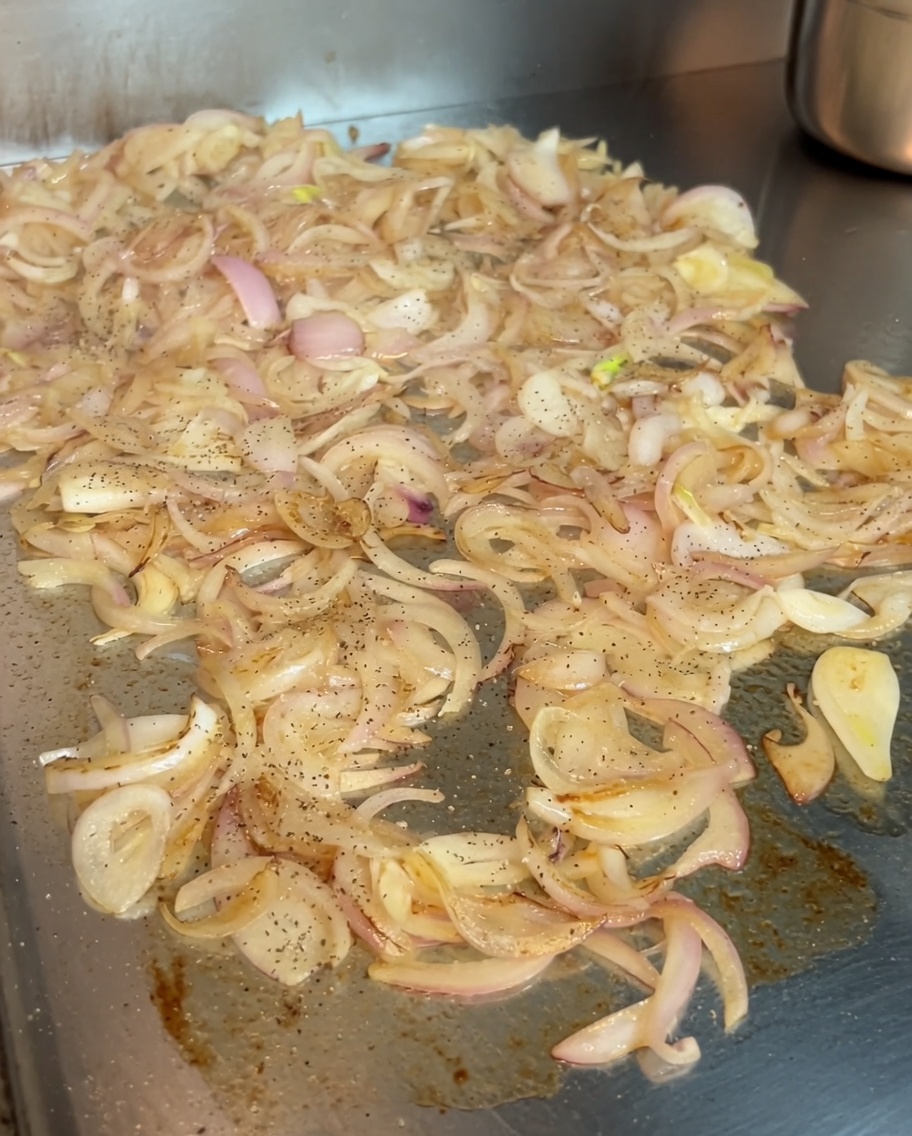 Karamellisierende Zwiebeln werden mit einer Prise schwarzem Pfeffer und ungarischem Edelsüßer Paprika bestreut.