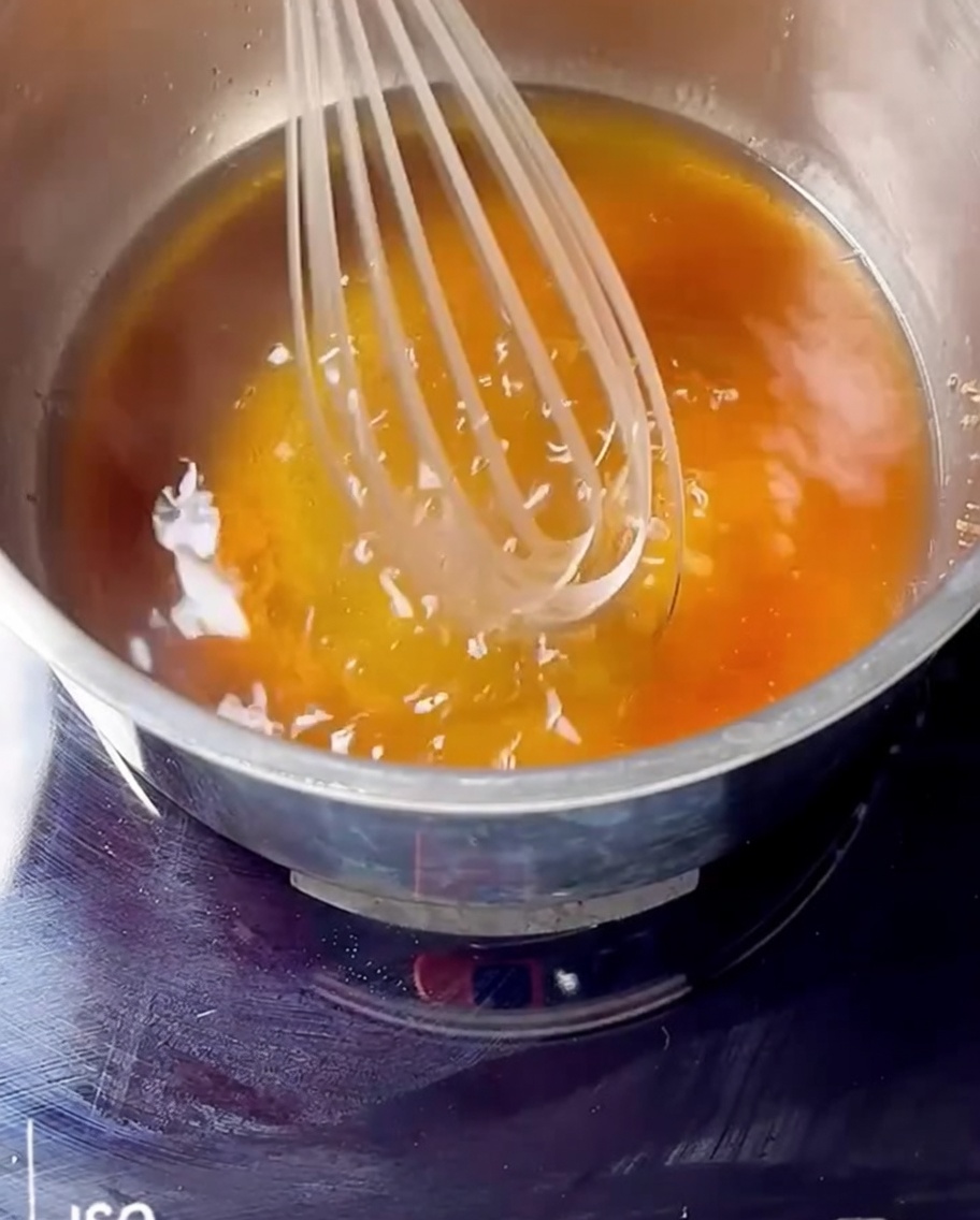 Ein Schneebesen verrührt Kirschmarmelade, Bourbon und braunen Zucker in einem Topf auf dem Herd.