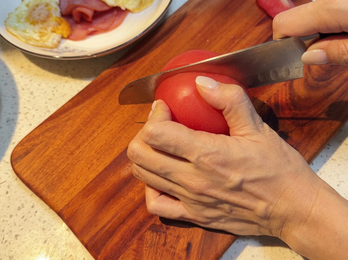 Frische Tomaten werden auf einem Holzbrett in gleichmäßige Scheiben geschnitten.