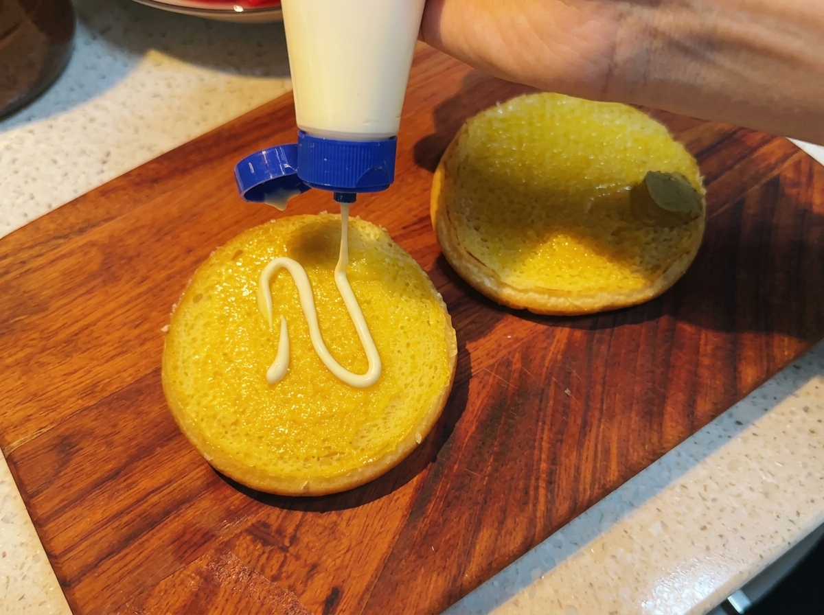 Mayonnaise wird auf das bereits mit Honigsenf bestrichene Brötchen gegeben.