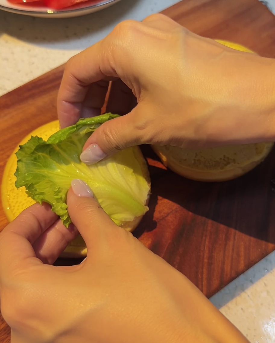Frische grüne Salatblätter werden vorsichtig auf das untere Brötchen gelegt.