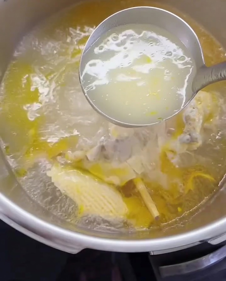 Eine Schöpfkelle gibt Hühnerbrühe und Fleisch in einen Topf.