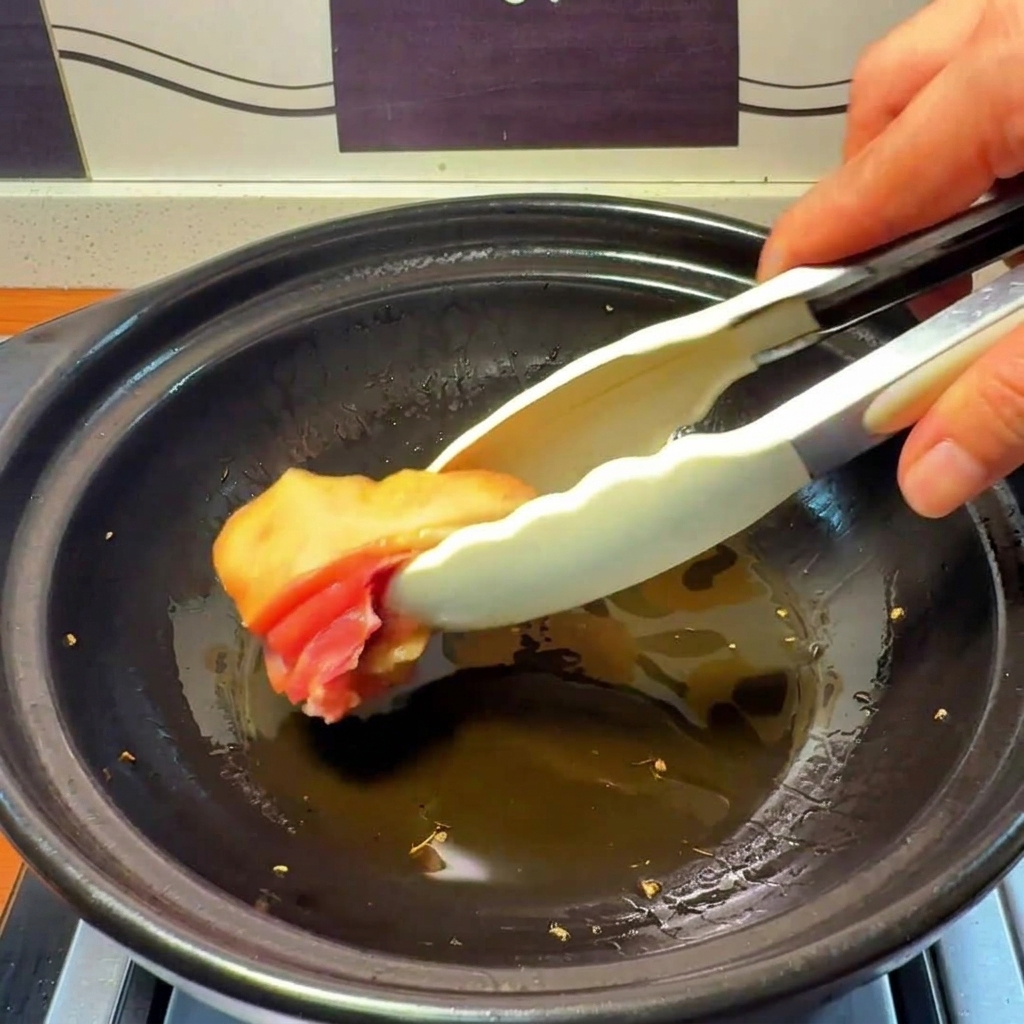 Rohe Hühnchenstücke werden in einen Tontopf mit heißem, mit Ingwer aromatisiertem Öl gelegt.