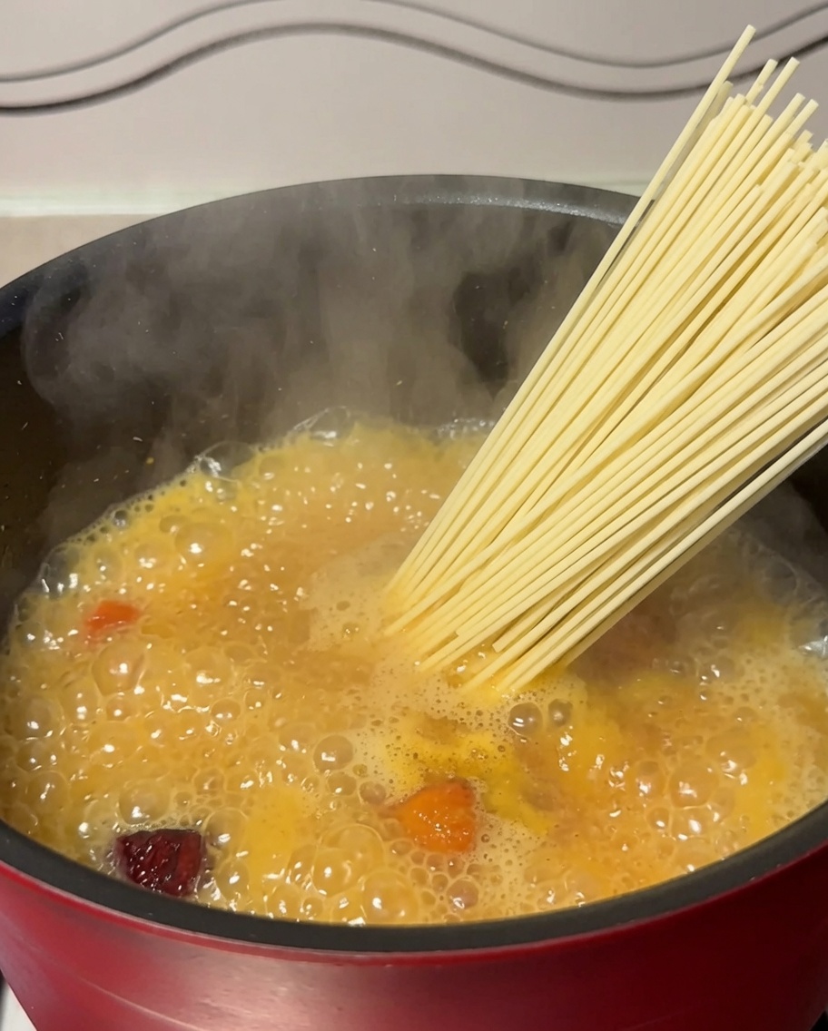 Getrocknete Nudeln werden in einen Topf mit kochender Hühnersuppe gegeben.