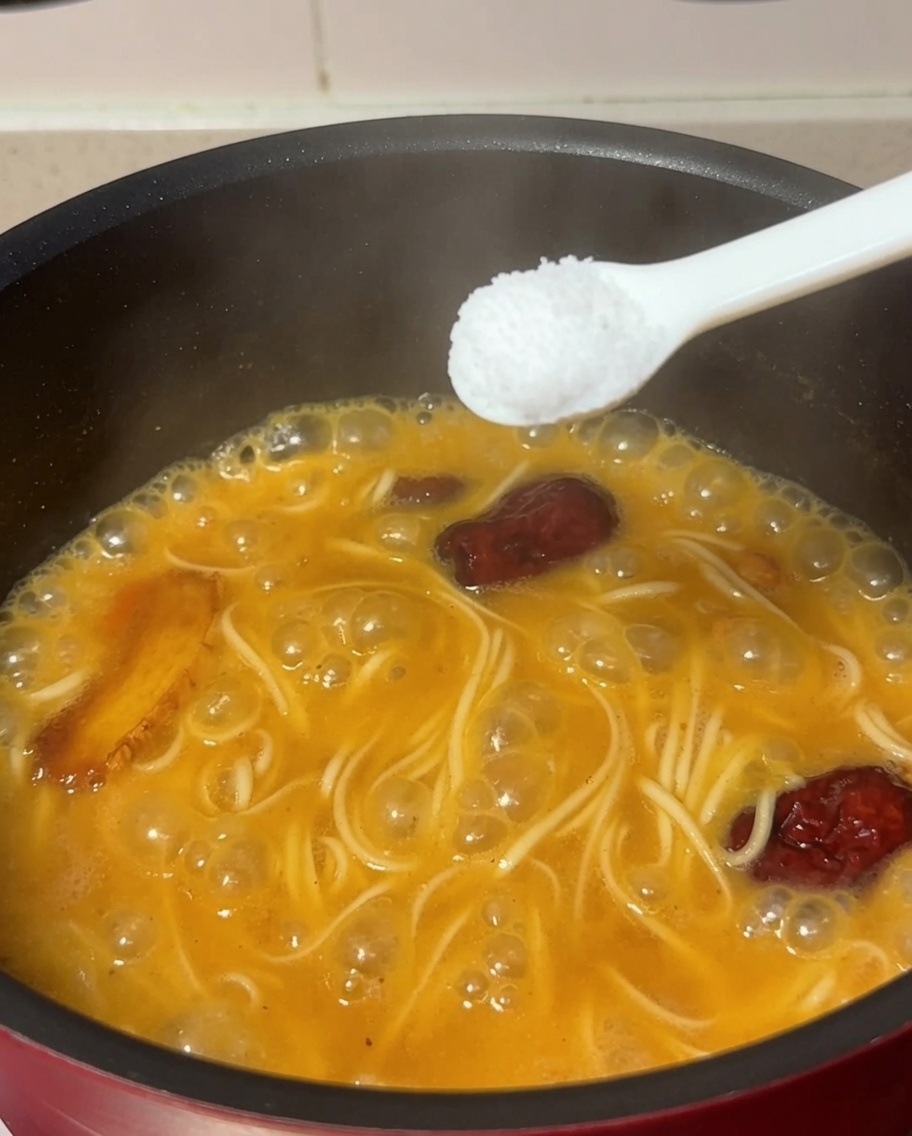 Ein Löffel Salz wird in den Topf mit kochenden Nudeln und Hühnersuppe gegeben.