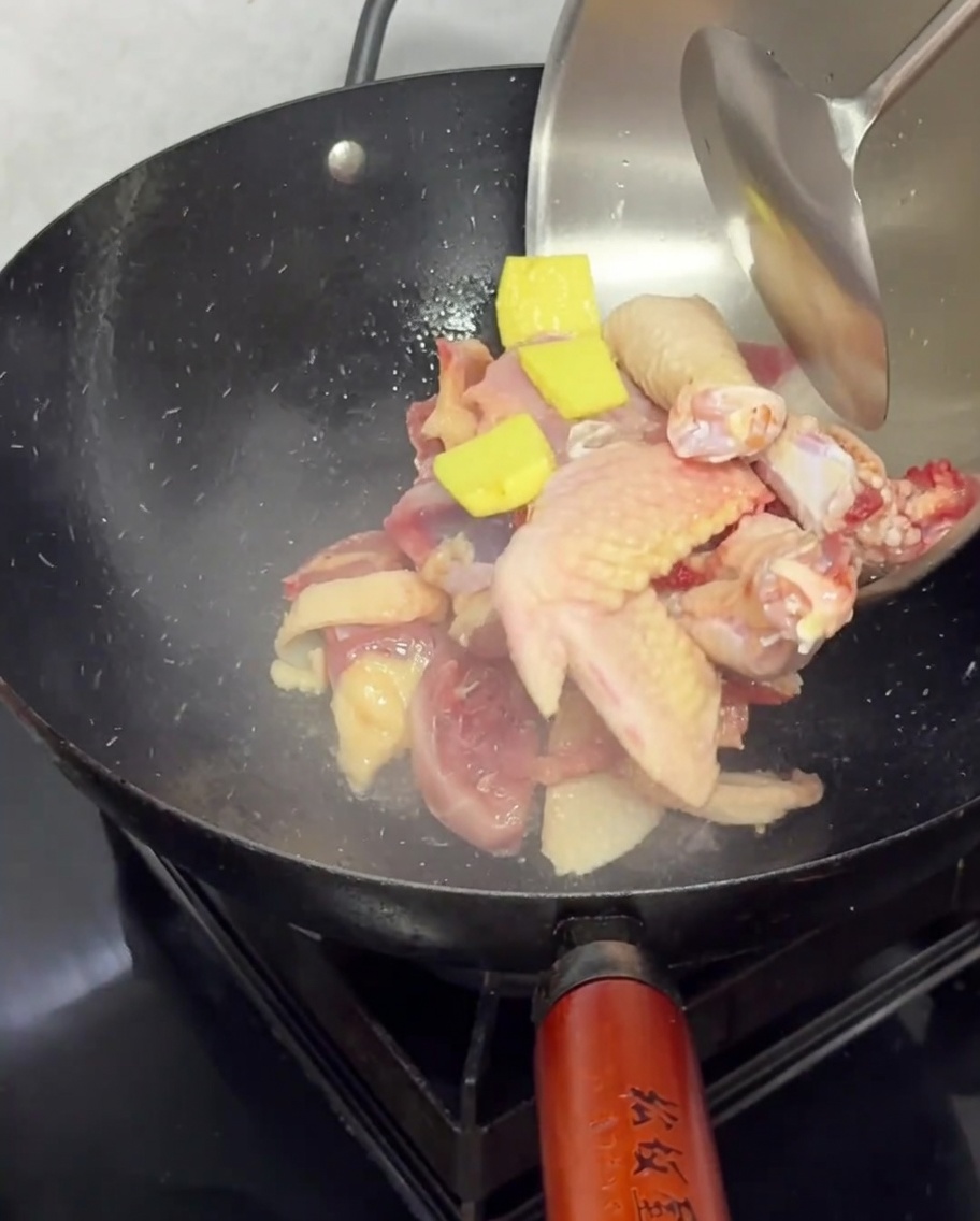 Rohe Hühnerstücke und Ingwerscheiben, die zum Anbraten in einen heißen schwarzen Wok gegeben werden.