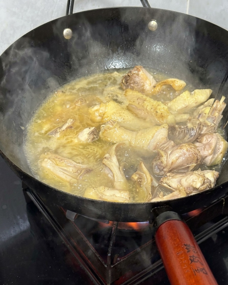 Hühnerstücke köcheln in einem Wok, der mit einer goldenen, blubbernden heißen Brühe gefüllt ist.