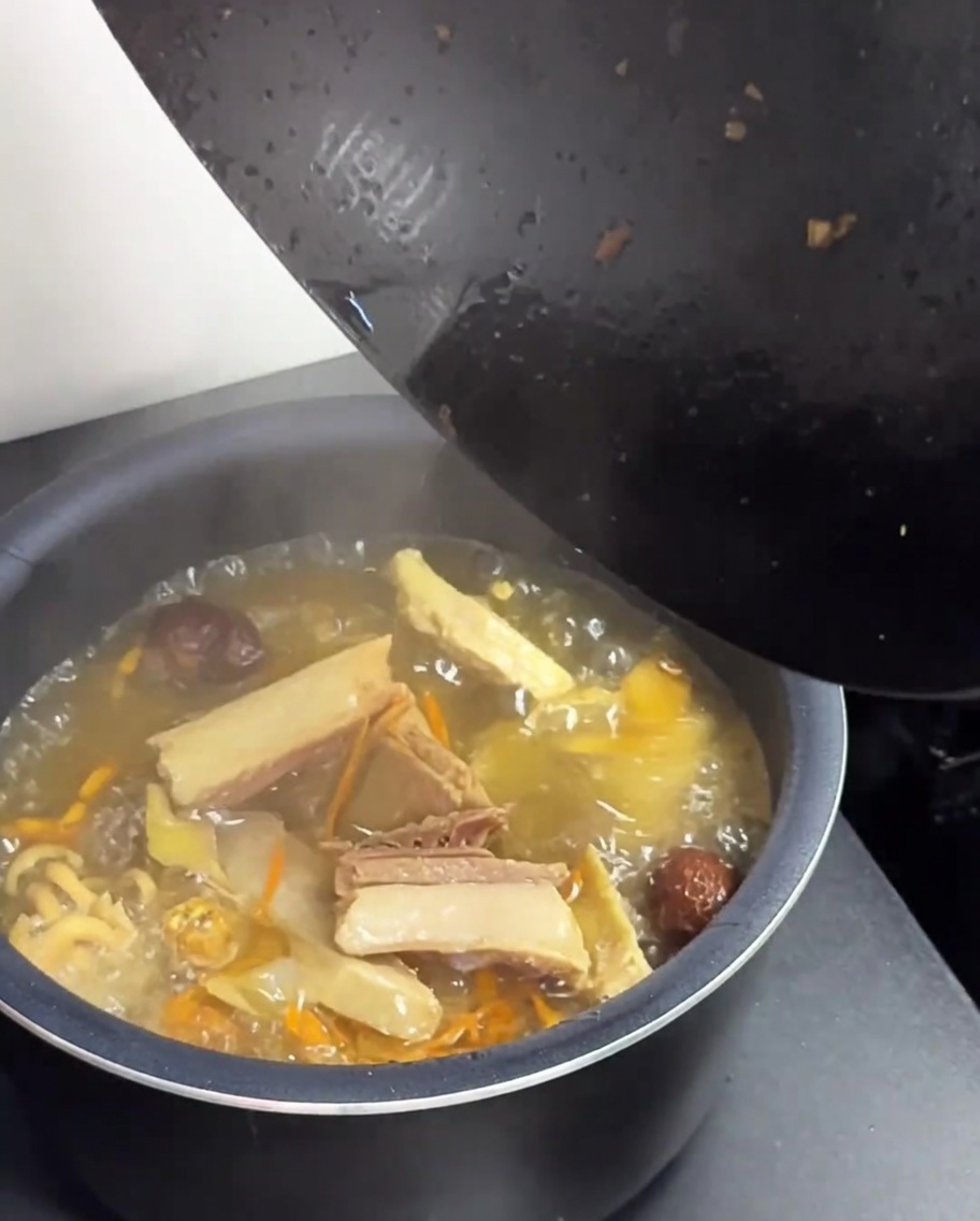 Die heiße Hühner-Pilz-Suppe wird von einem schwarzen Wok in einen grünen Reiskocher umgefüllt.