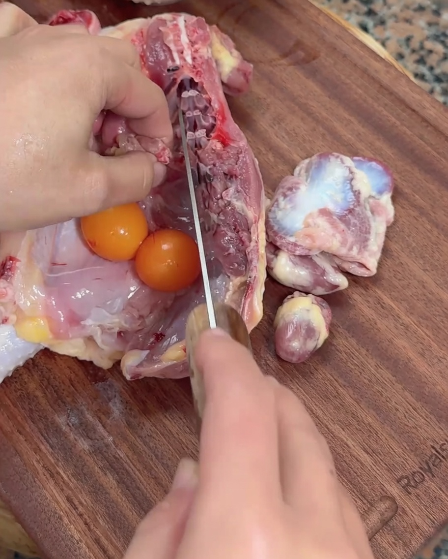 Hände ritzen rohe Hühnerinnereien und unfertige Eier mit einem Hackbeil auf einem Holzschneidebrett ein.
