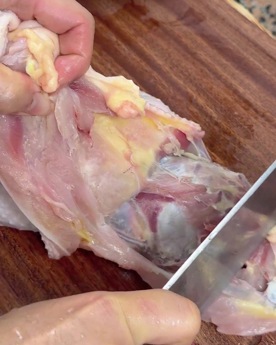 Hände halten ein rohes Hähnchen und lösen das Fleisch mit einem Messer von der Karkasse.