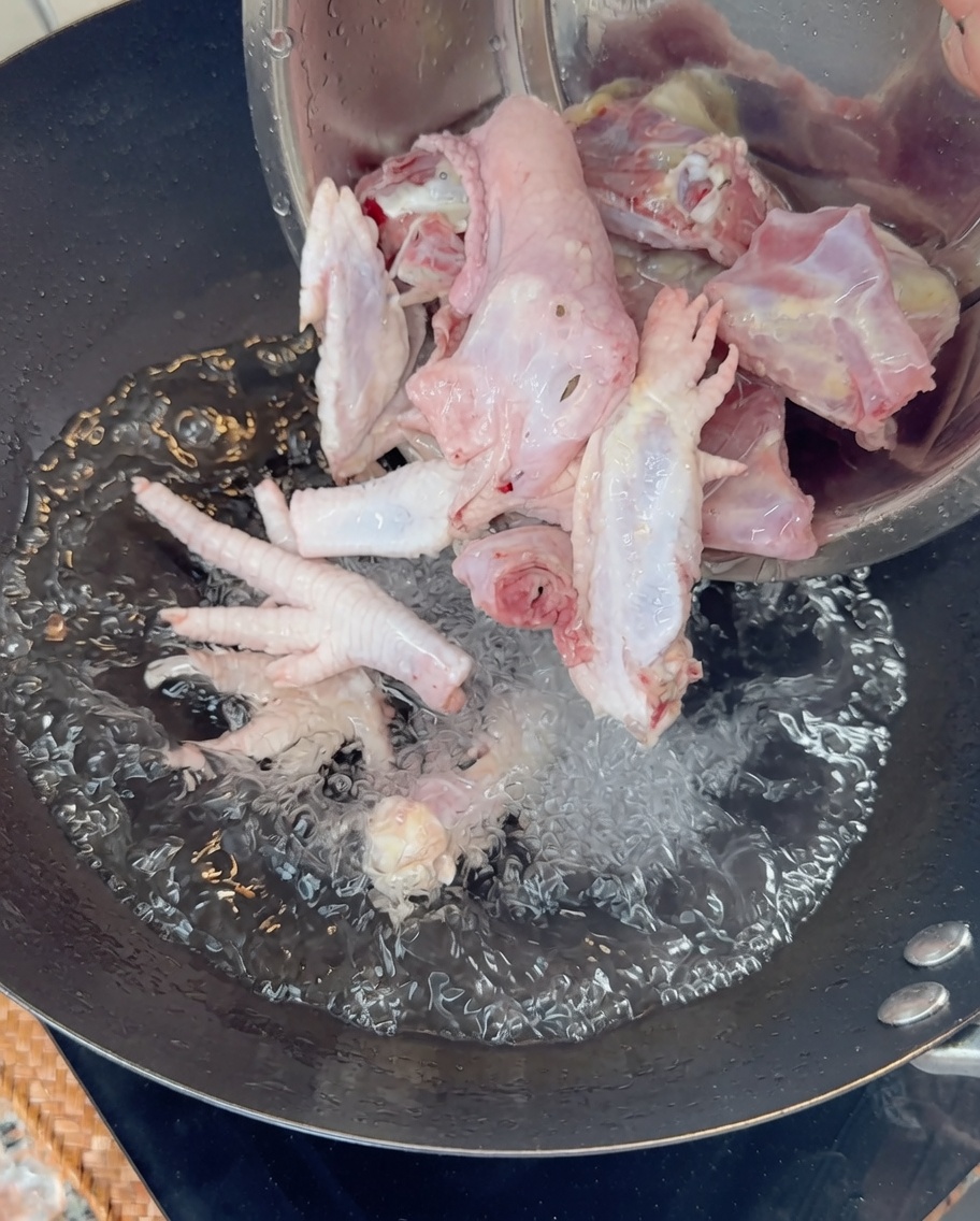 Rohe Hühnerknochen und Füße werden in einen Wok mit kochendem Wasser gegeben.