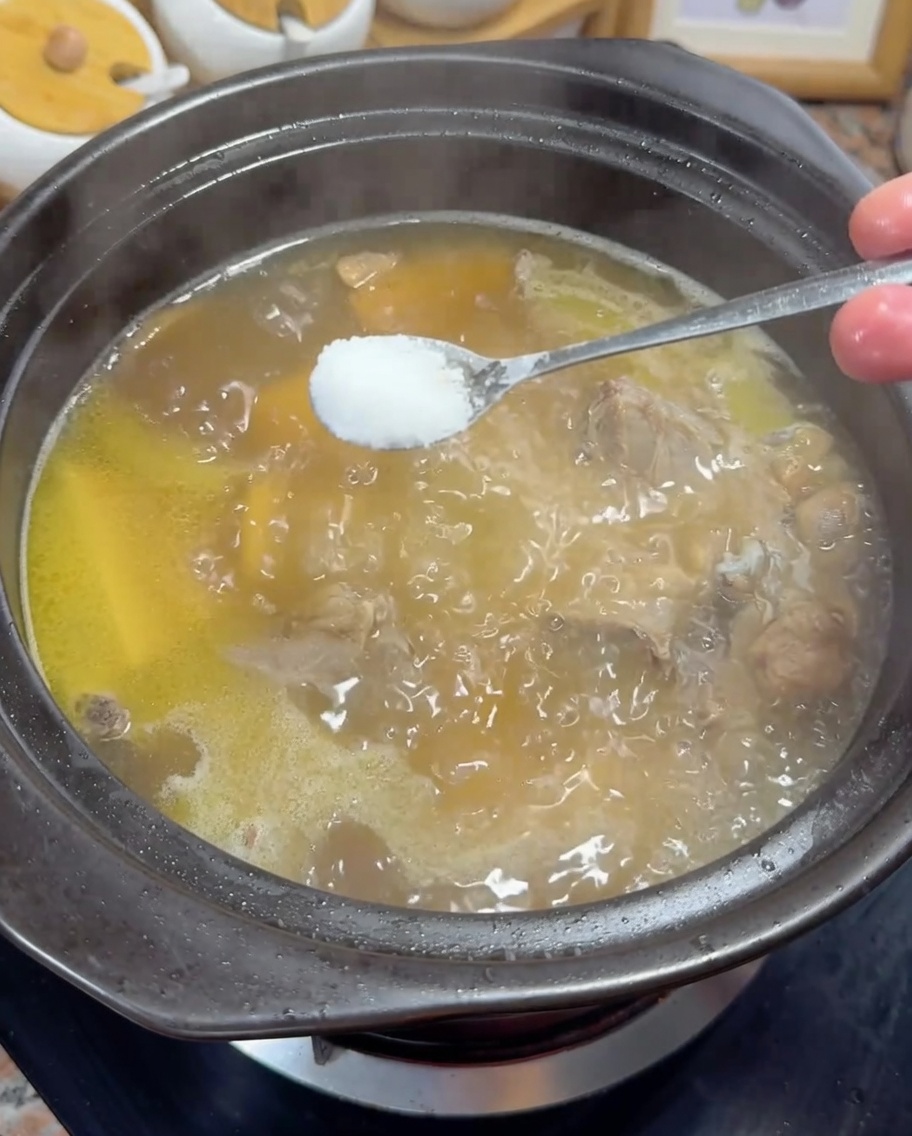 Ein Löffel weißes Salz wird in eine köchelnde goldene Hühnerbrühe gegeben.
