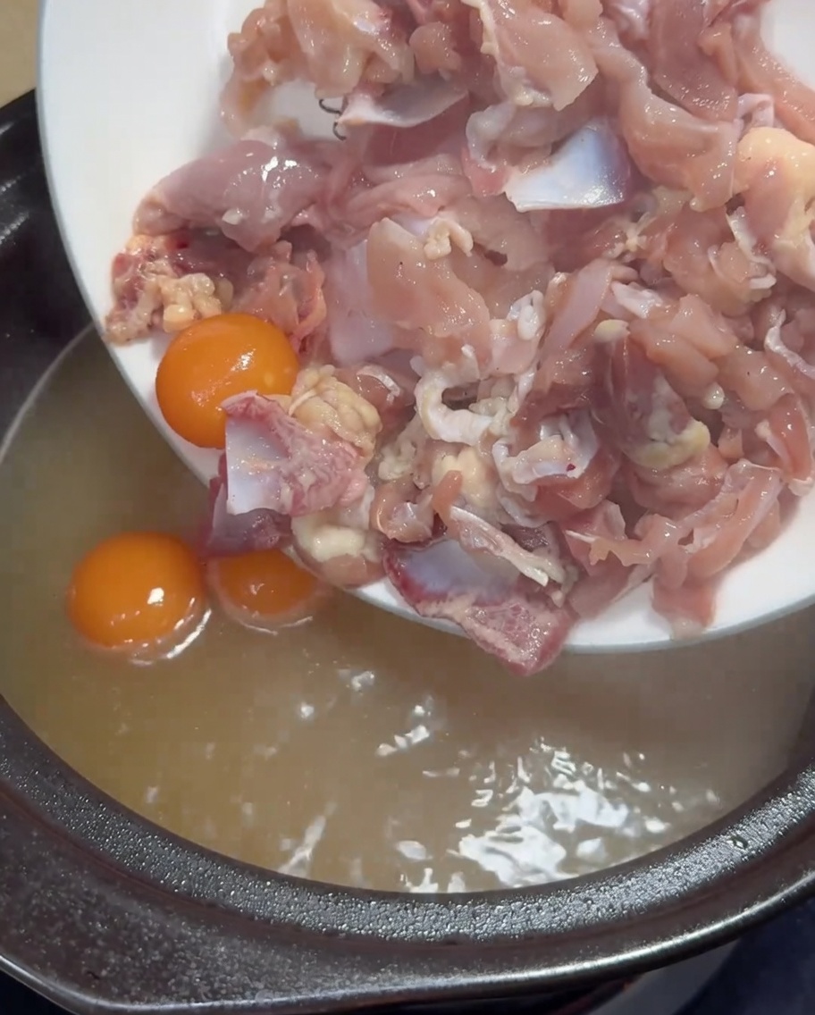 Dünn geschnittenes rohes Hähnchenfleisch und gelbe Eigelbe werden in einen Topf mit kochender goldener Hühnerbrühe gegeben.