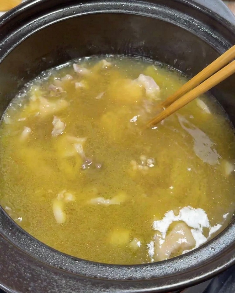 Essstäbchen rühren sanft Hühnerstreifen und Eigelb in der köchelnden Suppe um.