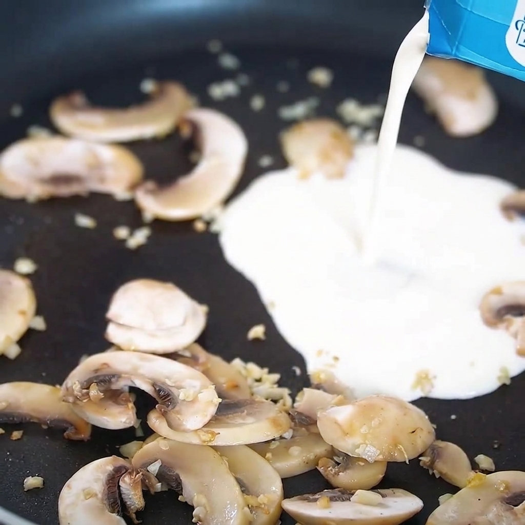 Sahne wird in eine Pfanne mit gebratenen Pilzen und Knoblauch gegossen.
