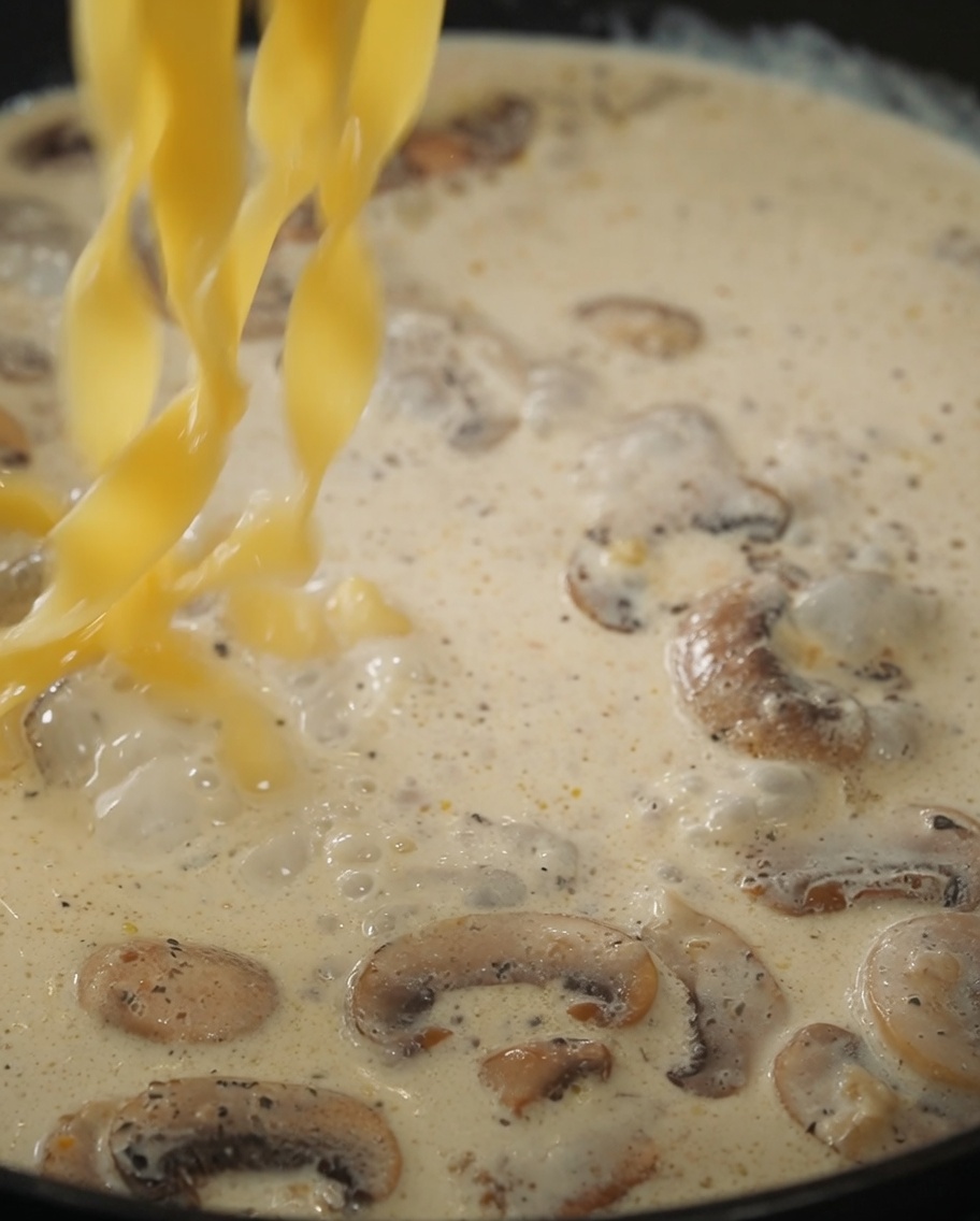 Nudeln und schwarze Trüffelsauce werden mit der Pilz-Sahnesauce in der Pfanne vermischt.