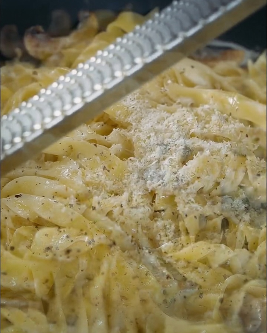 Hartkäse wird frisch über eine Pfanne voller cremiger Trüffel-Pasta gerieben.