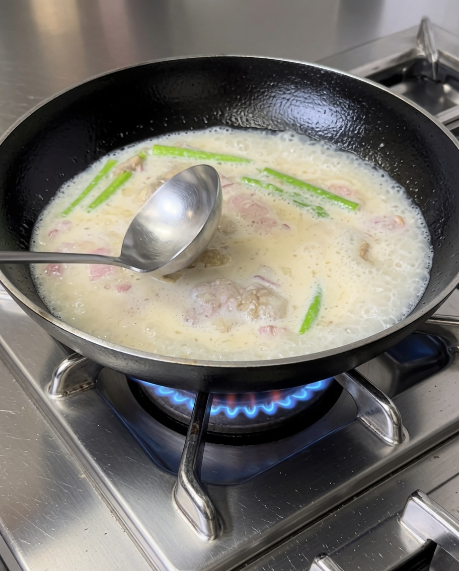 Gekochte Penne-Nudeln werden unter die cremige Speck-Gemüse-Sauce in der Pfanne gehoben.
