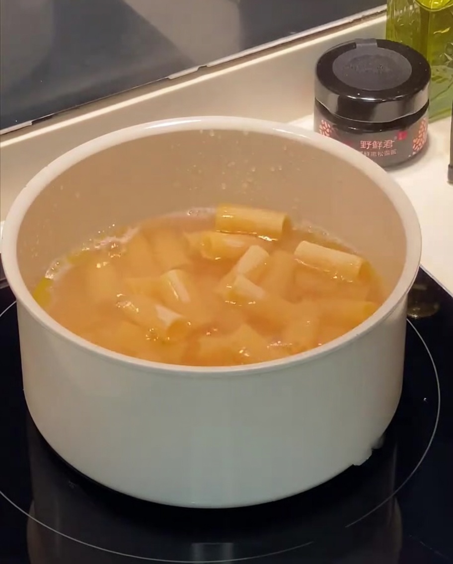 Rigatoni kochen in einem Topf mit Wasser, sichtbare Blasen und Öltröpfchen an der Oberfläche.