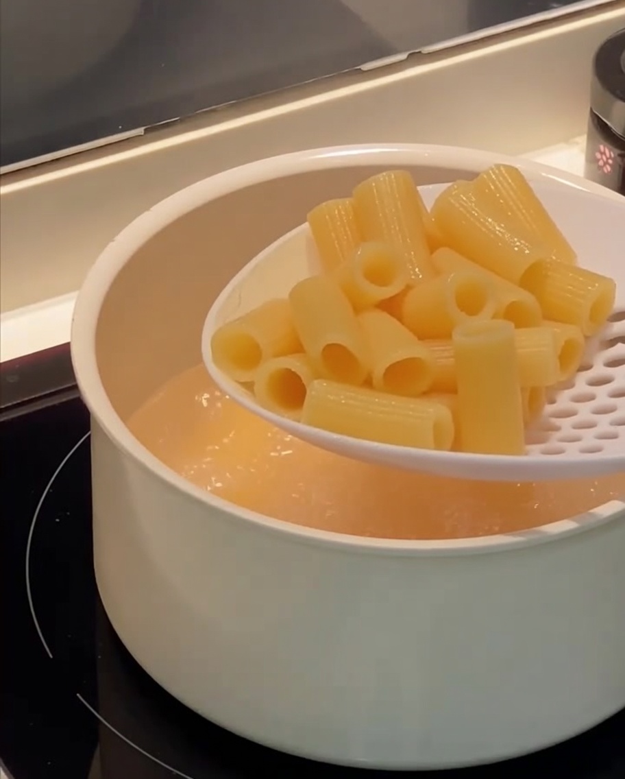 Ein Schaumlöffel hebt gekochte Rigatoni aus einem Topf mit kochendem Wasser.