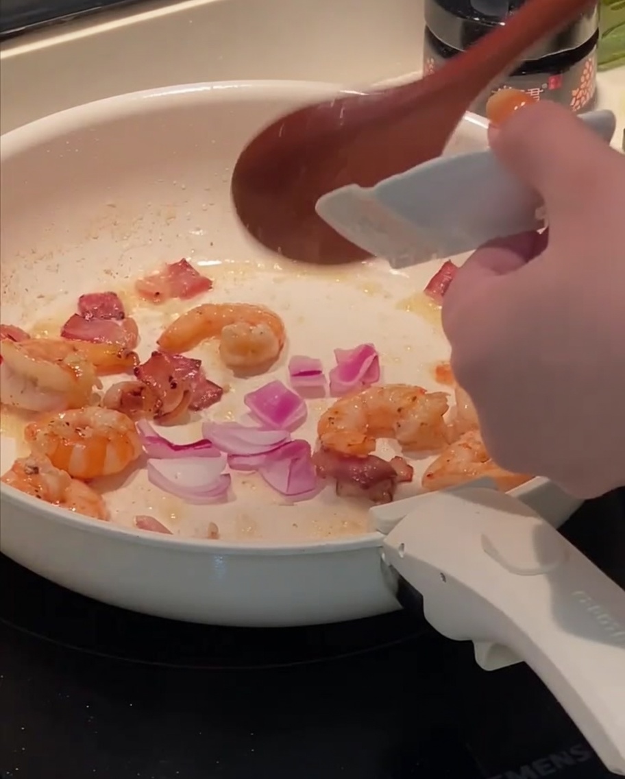 Gehackte Zwiebeln kommen in die Pfanne zu Speck und Garnelen.