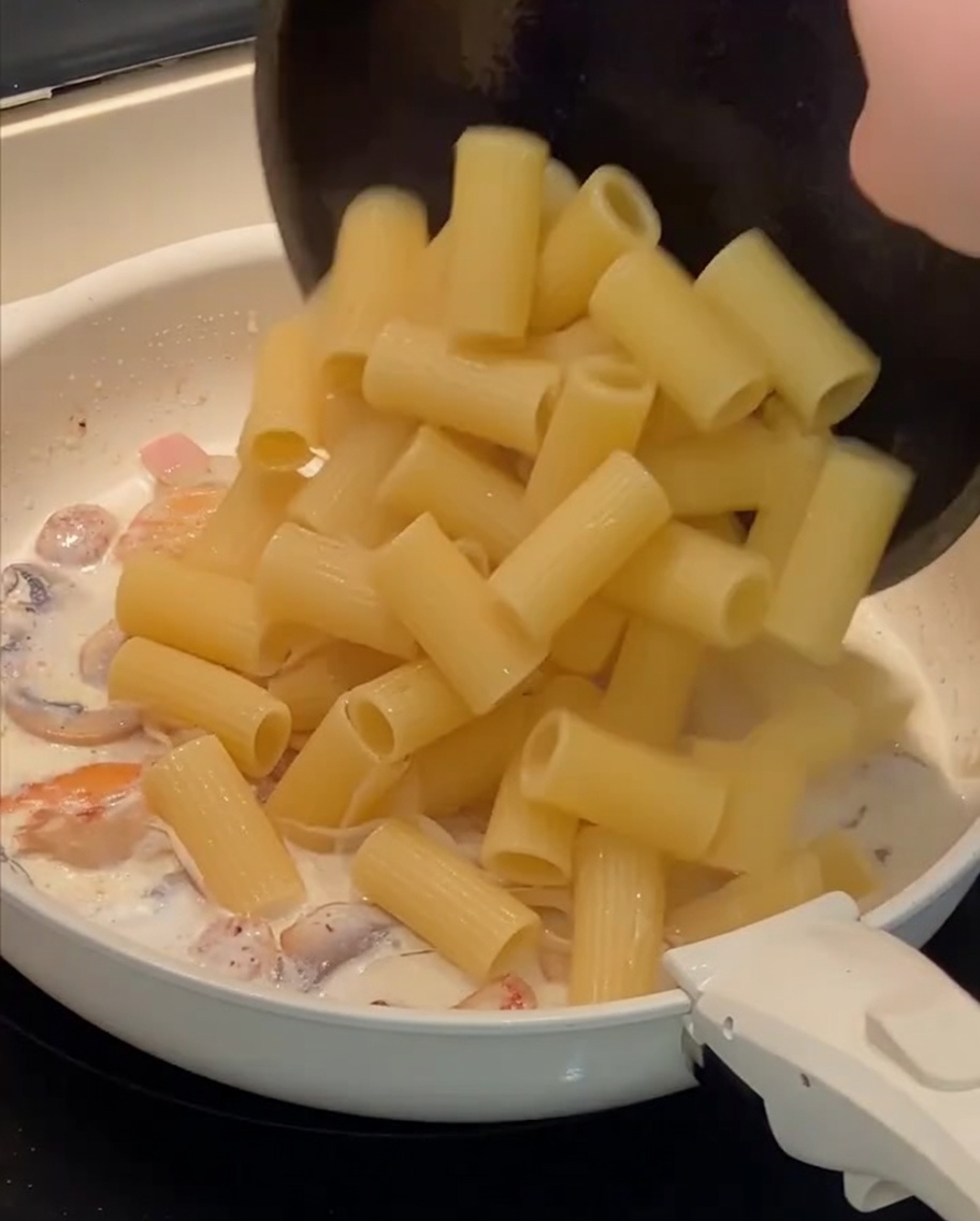 Gekochte Rigatoni werden in die Pfanne zur cremigen Sauce gegeben.