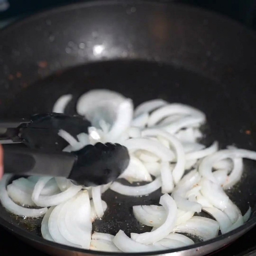 Durchscheinende Zwiebelstreifen, die im klaren goldenen Speckfett angebraten werden.