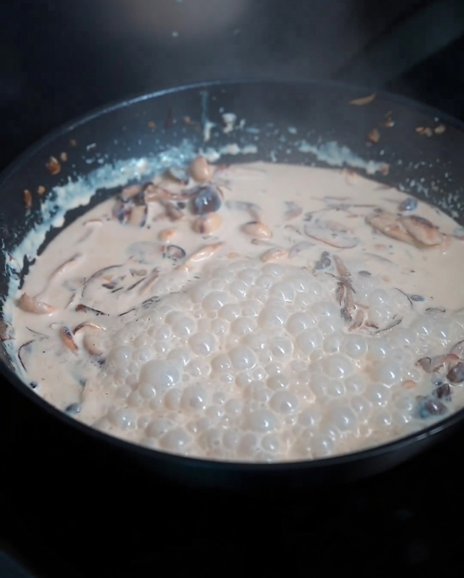 Gekochte Nudeln werden in die reichhaltige Pilzsauce in der Pfanne geschwenkt.