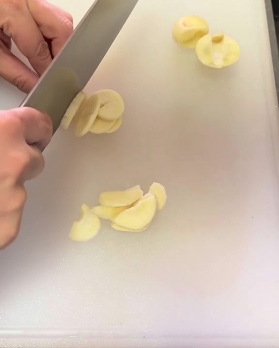 Fein geschnittene Knoblauchscheiben sind auf einem weißen Schneidebrett verteilt.