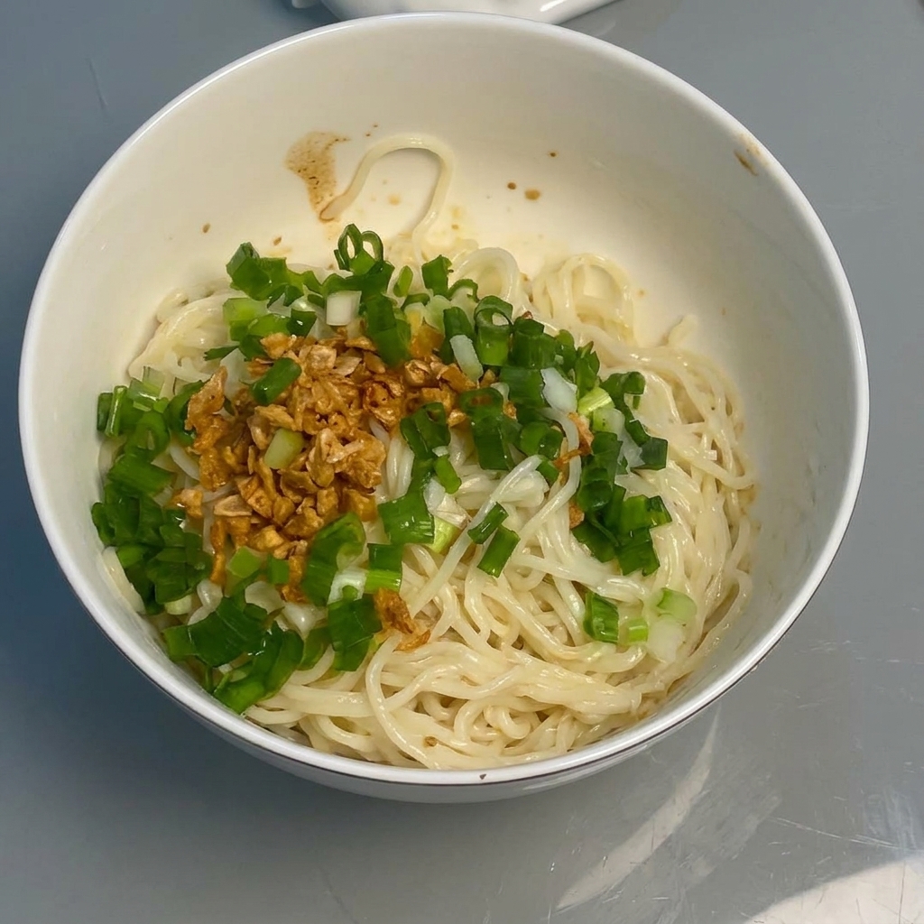 Nudeln werden mit Essstäbchen mit Sauce, Knoblauch und Zwiebeln vermischt.