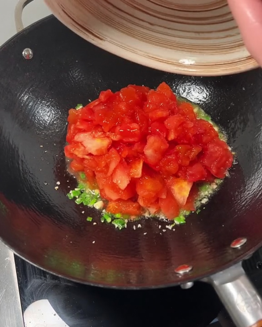 Gewürfelte Tomaten werden zu den Frühlingszwiebeln und dem Knoblauch in den Wok gegeben.