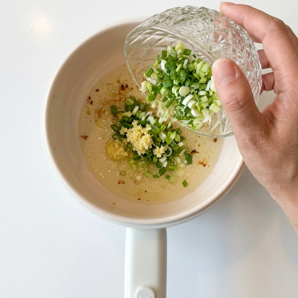 Gehackte Frühlingszwiebeln werden in den Topf mit dem angebratenen Knoblauch gegeben.