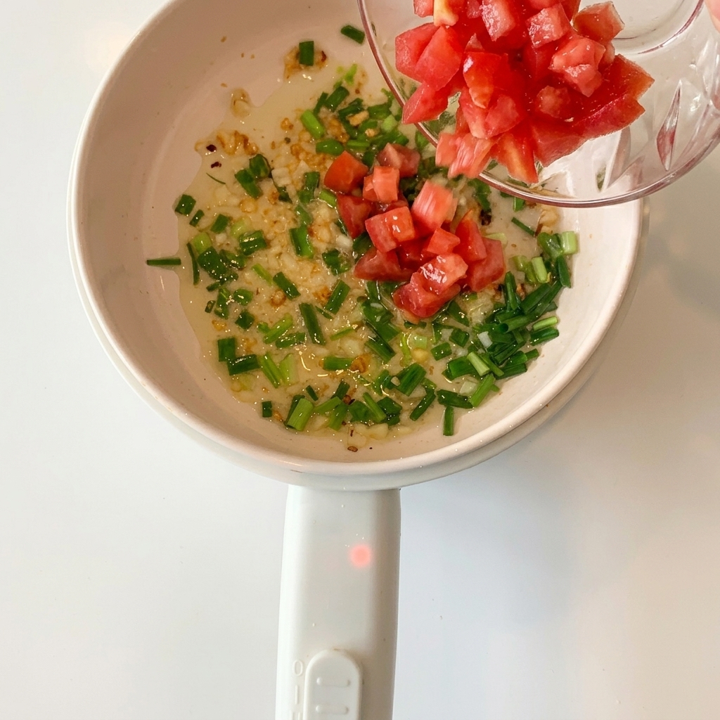 Gewürfelte rote Tomaten werden in den Topf mit Knoblauch und Frühlingszwiebeln gegeben.