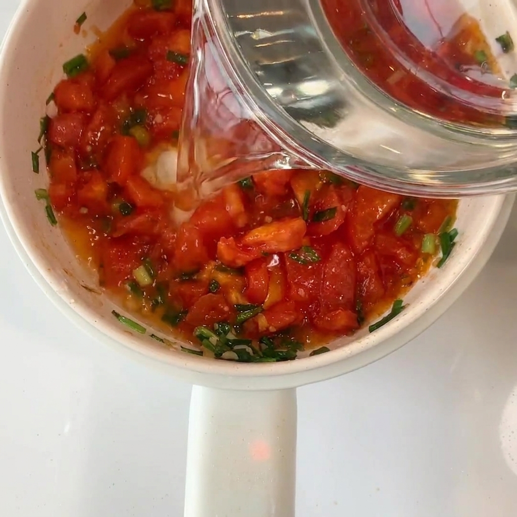 Klares Wasser wird aus einer Glasschüssel in den Topf mit den Tomaten gegossen.