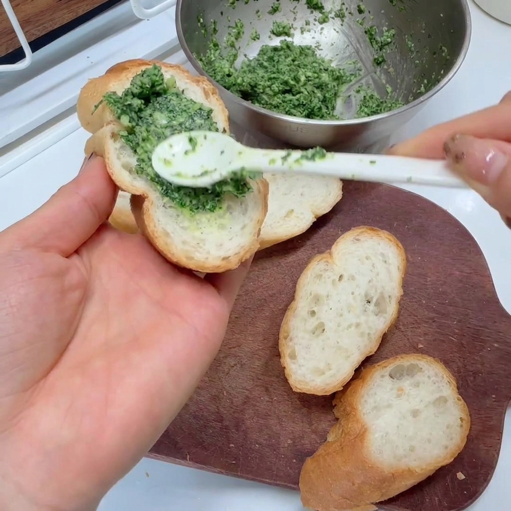 Die grüne Knoblauch-Petersilien-Mischung wird mit einem Löffel auf die Baguettescheiben aufgetragen.