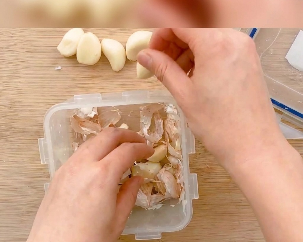 Geschälte Knoblauchzehen werden auf einem Holzbrett in dünne Scheiben geschnitten.